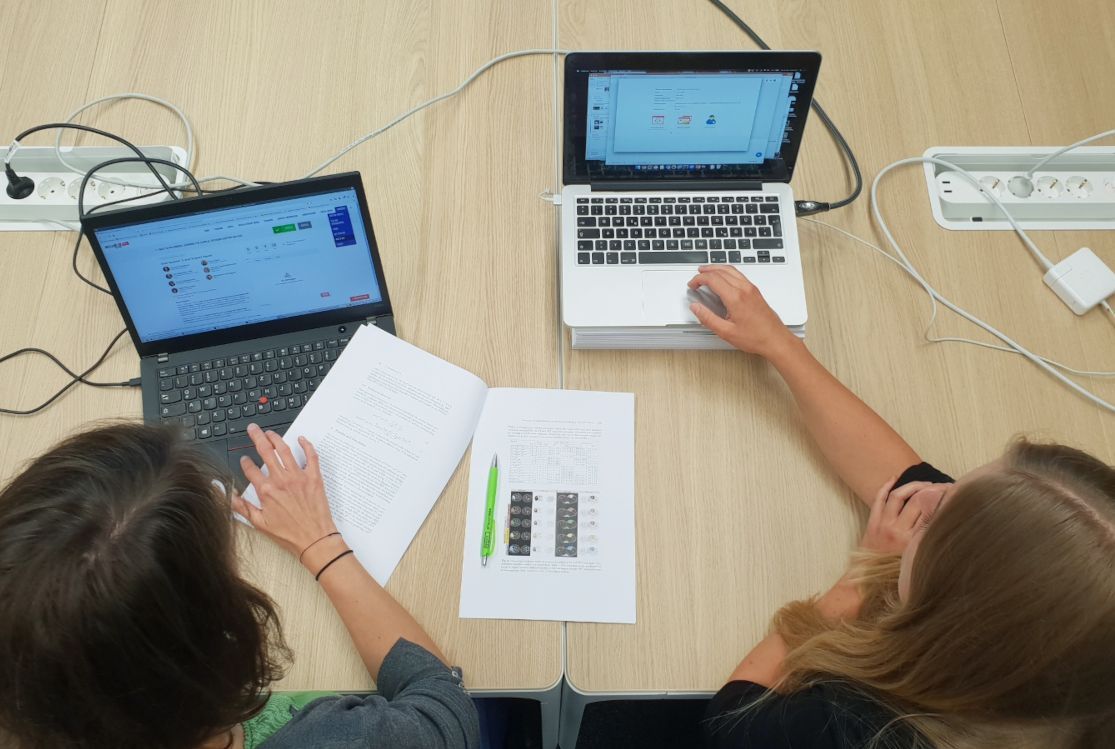 Blick von oben auf zwei Forscherinnen, die gemeinsam an einem Tisch vor zwei Laptops sitzen und eine Publikation besprechen.