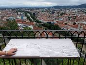 The tactile panoramic relief is clearly visible in front of the view from Graz Museum Schlossberg, with one hand resting on the relief.